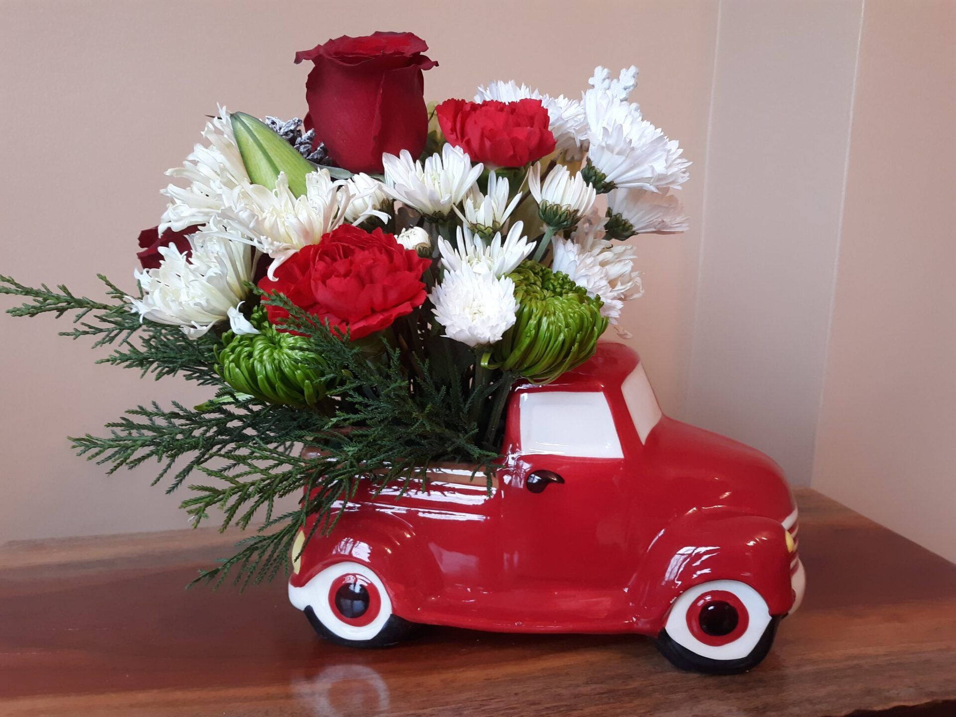A red truck filled with flowers is sitting on a wooden table.