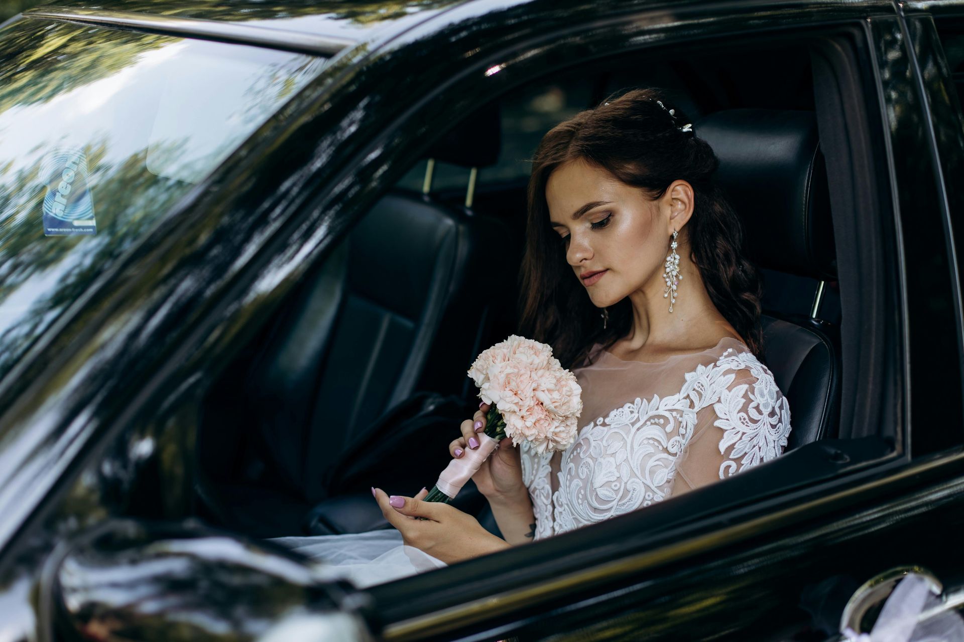 A bride is sitting in the back seat of a car holding a bouquet of flowers.