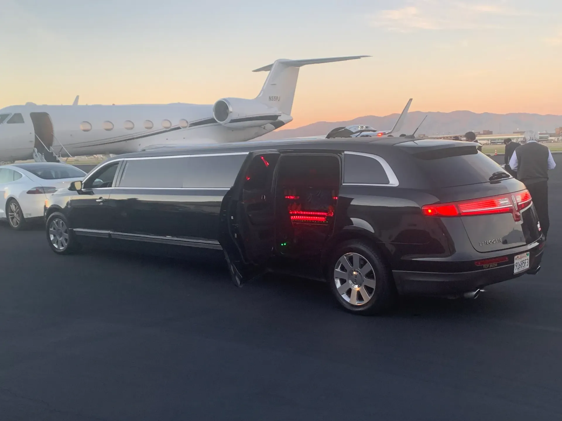 A black limousine is parked in front of a private jet.