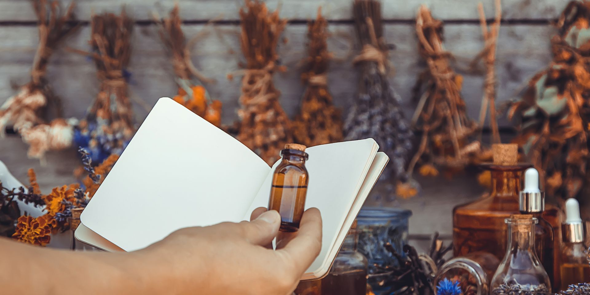 A person is holding a bottle of essential oil in their hand while reading a book.