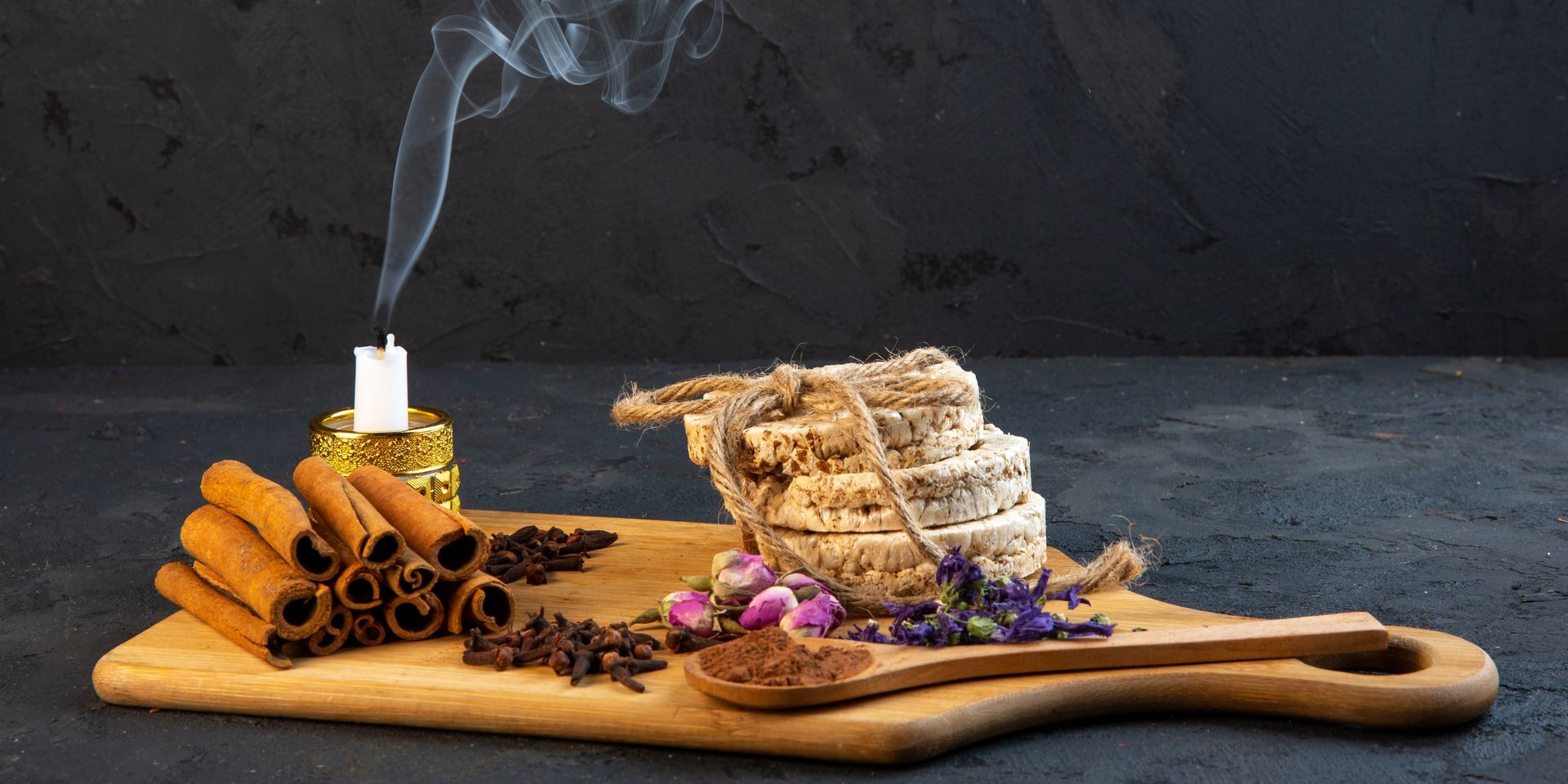 There is smoke coming out of a candle on a wooden cutting board.
