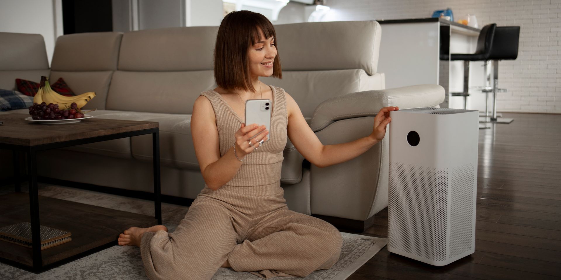 A woman is sitting on the floor in front of a air purifier.