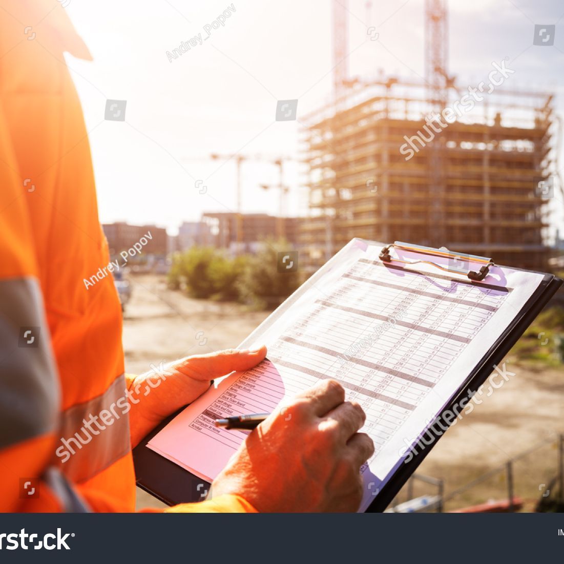 A construction worker is holding a clipboard and writing on it.