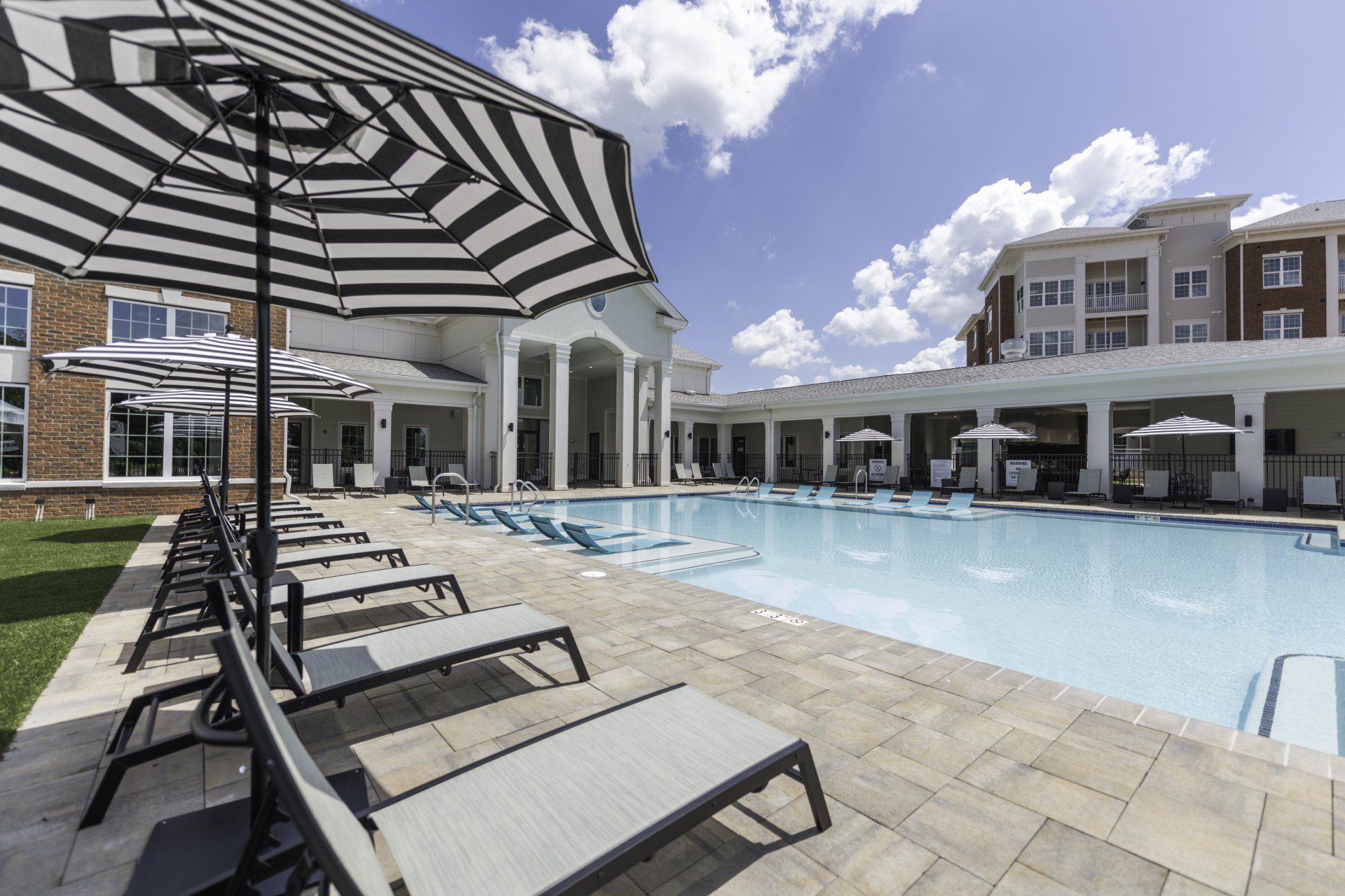 A large swimming pool surrounded by chairs and umbrellas in front of a building.