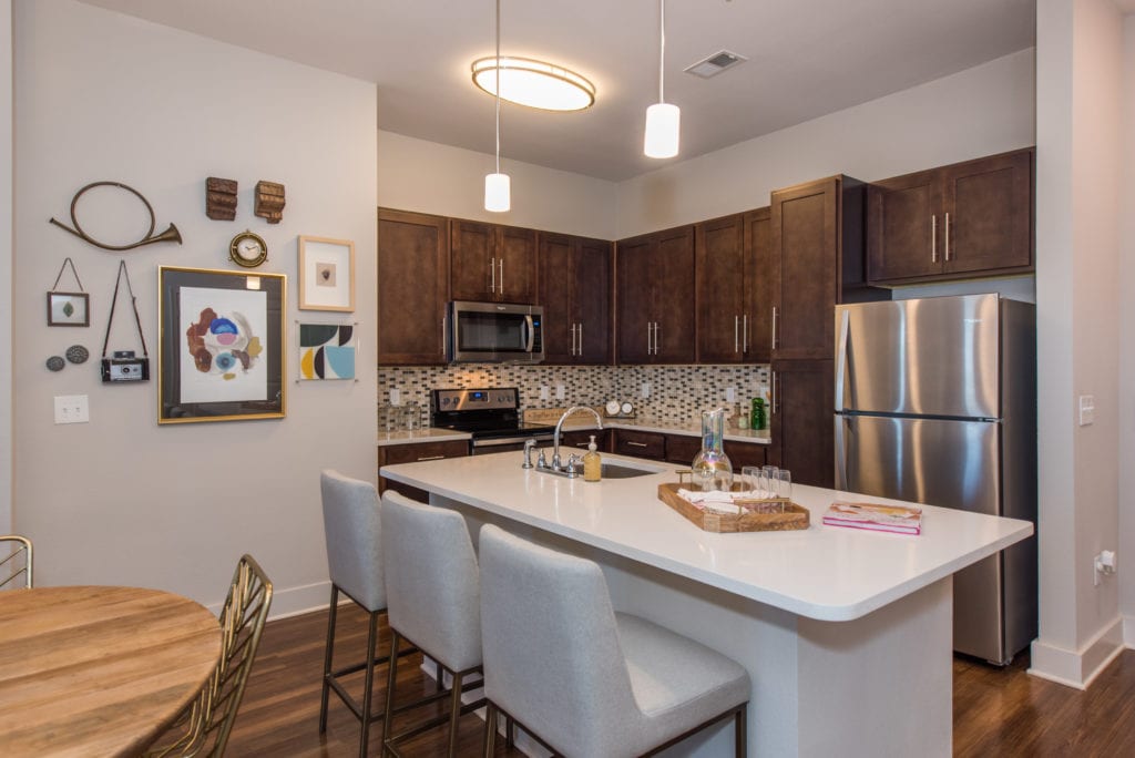 A kitchen with stainless steel appliances , wooden cabinets , a table and chairs.
