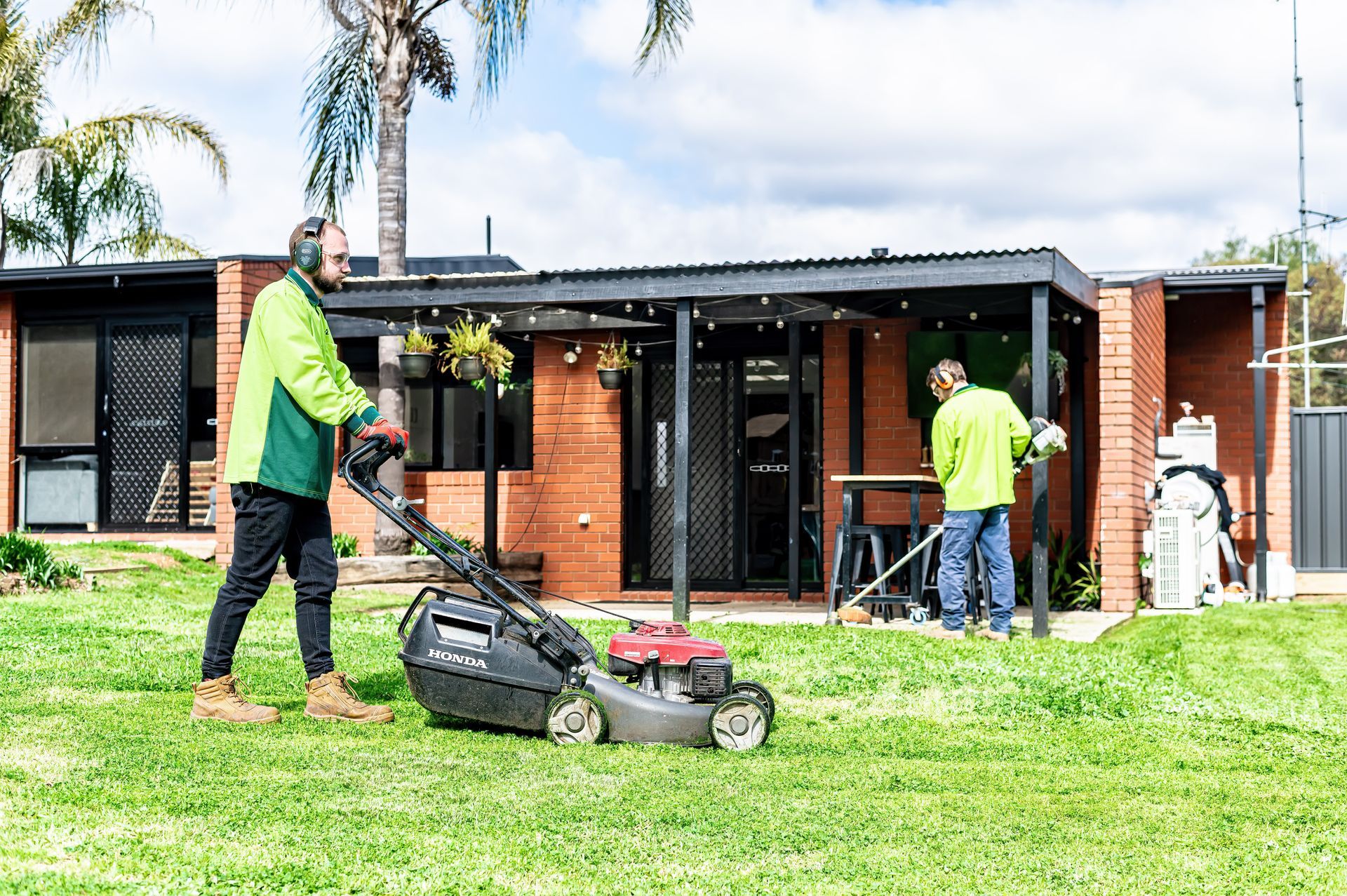 A Man Is Using A Lawn Mower To Cut The Grass In Front Of A House — 2easy Cleaning in Bendigo, VIC