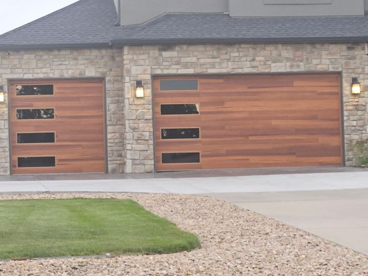 Two wood garage doors with horizontal windows on a stone house exterior.
