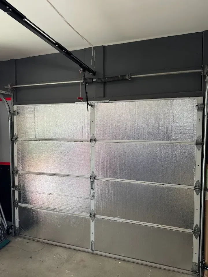 Closed insulated garage door with silver panels and black tracks in a gray-walled garage