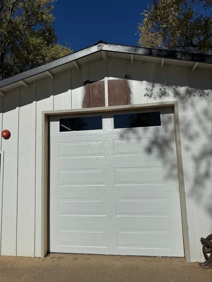 White garage door on a light-colored building under a blue sky, with a small window above the door.