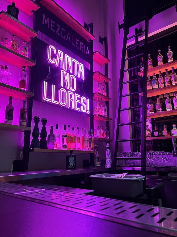 Interior of a bar with shelves of bottles and neon sign in purple light.