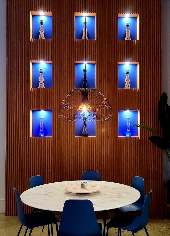 Dining room with round table, blue chairs, and wooden wall with lit displays.