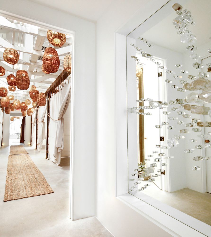 Bright, white hallway with open doorways. One leads to a room with hanging lights, the other a mirror decorated with glass.
