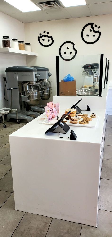A white cookie shop interior with cookie designs on the wall and cookies on display.