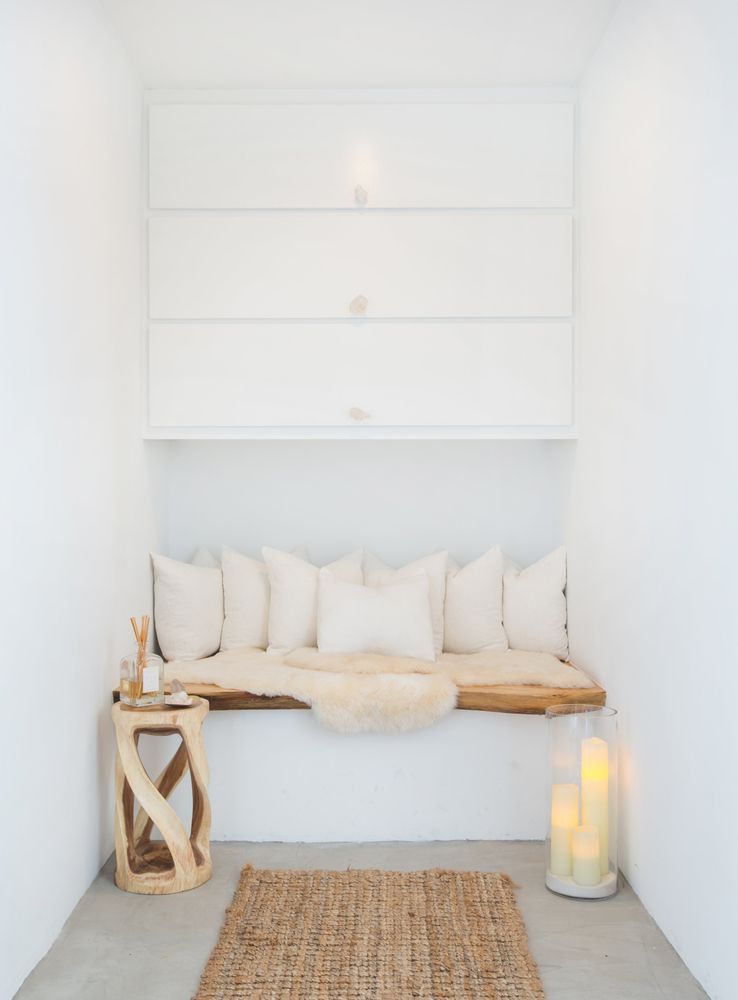 Cozy, white-walled alcove with a built-in bench, pillows, sheepskin rug, and candles.