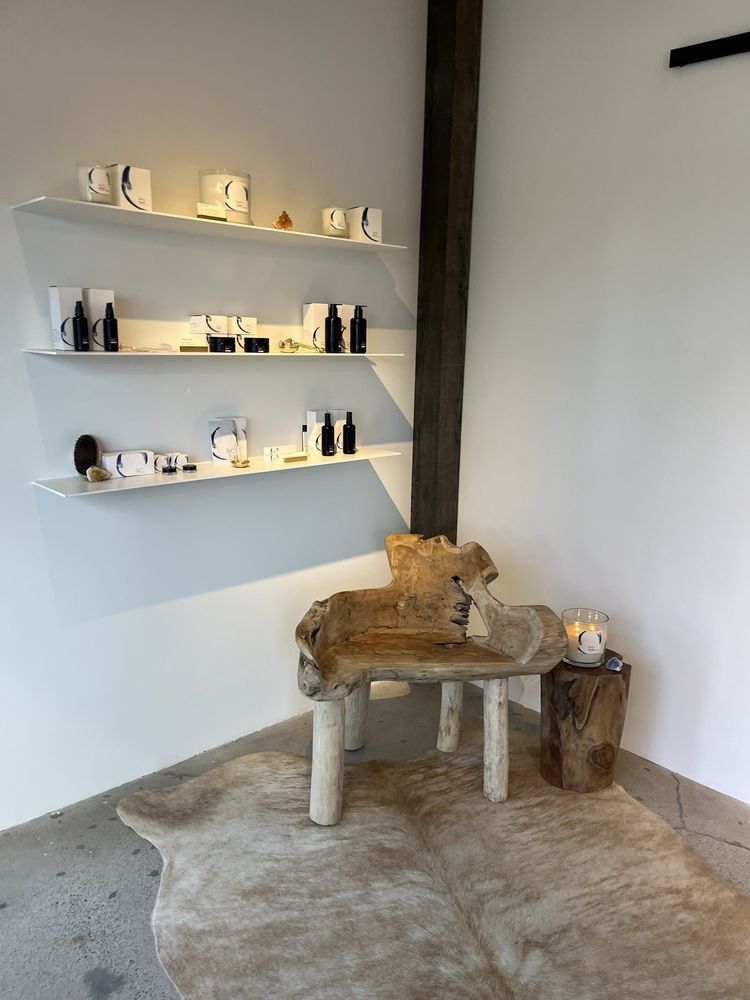 Corner display with white shelves of products, a rustic bench on a cowhide rug, and a tree stump table.