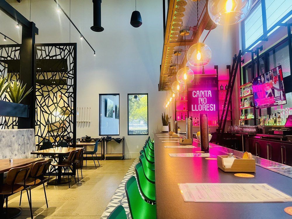 Restaurant interior: bar with neon sign, green seating, tables, and decorative cutouts. Bright and inviting.