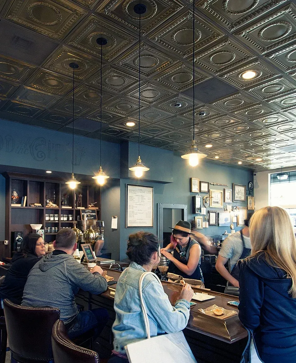 People at a bar with decorative ceiling, dark walls, and servers behind the bar.