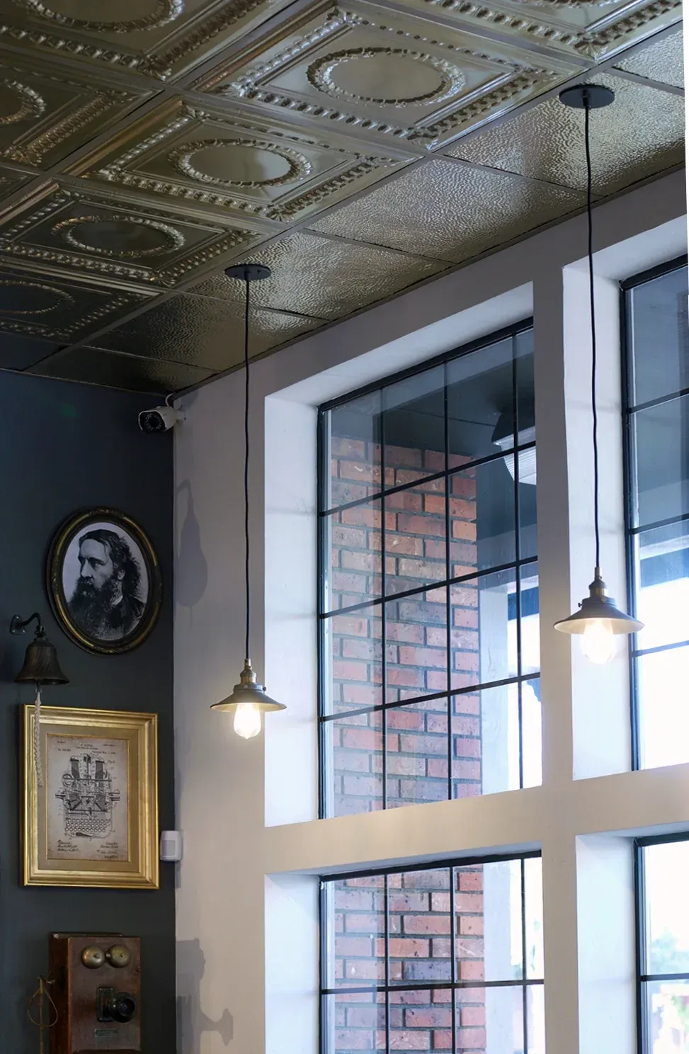 Interior with tin ceiling, large windows, brick wall, pendant lights, and framed art.