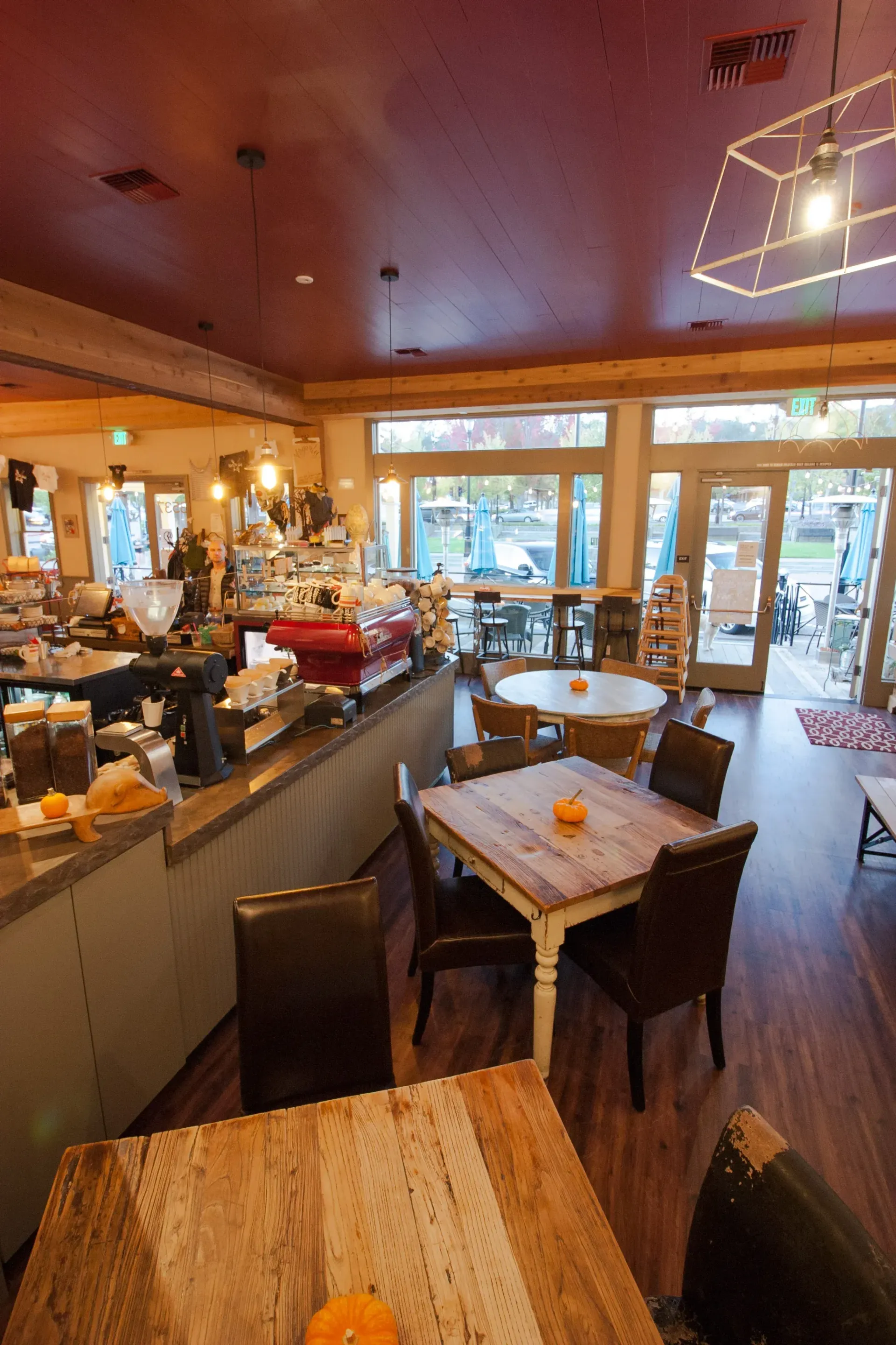 Interior of a cafe with tables and chairs, a coffee bar, and large windows, natural light.