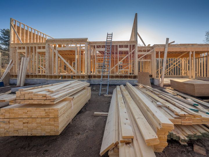 Wooden house frame under construction with lumber stacked in the foreground.