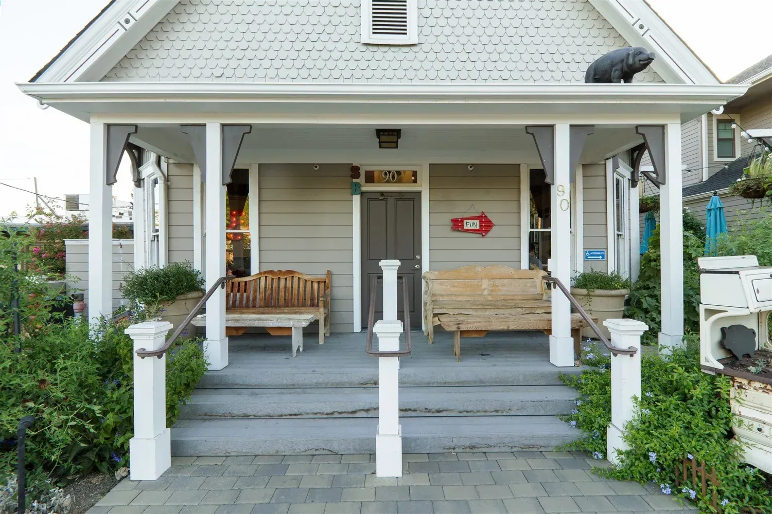 Cottage with porch, benches, and steps. Gray siding, white trim, red mailbox, and greenery.