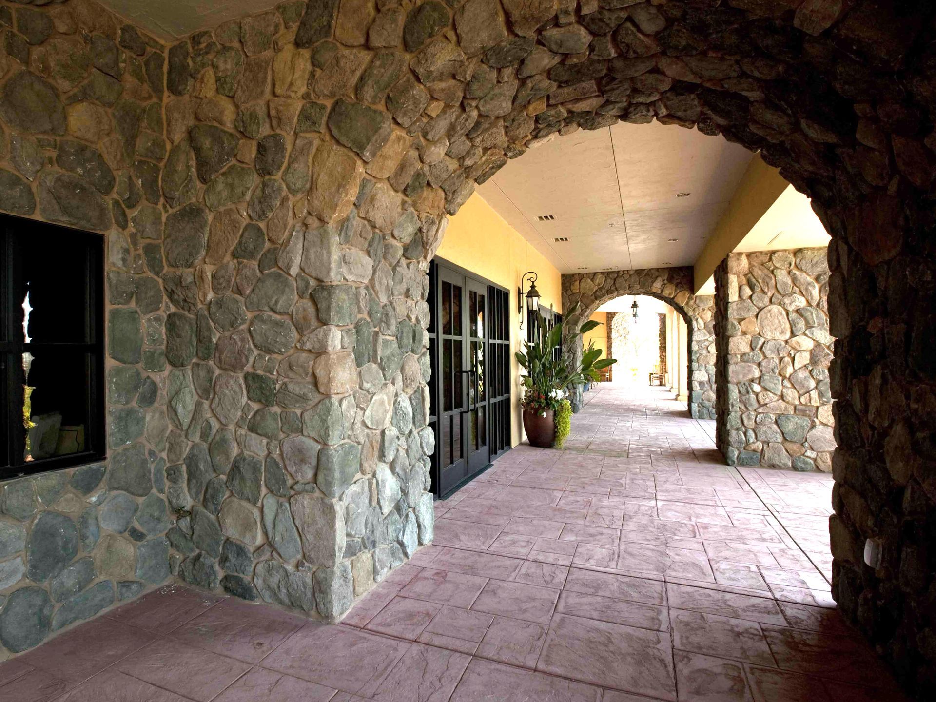 Stone archway with hallway, dark doors, and potted plant.