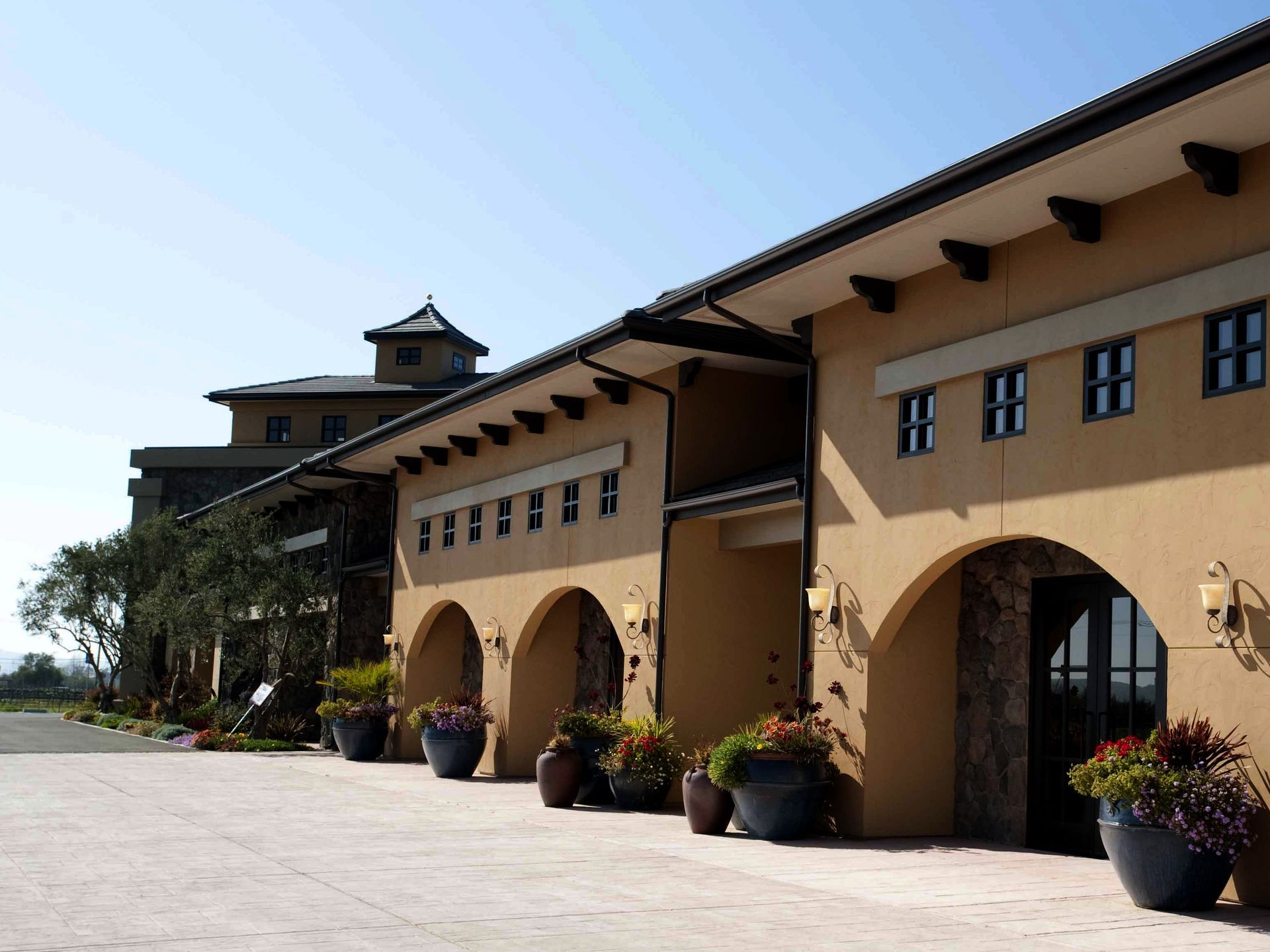 Tan building with arched entrances and potted flowers.