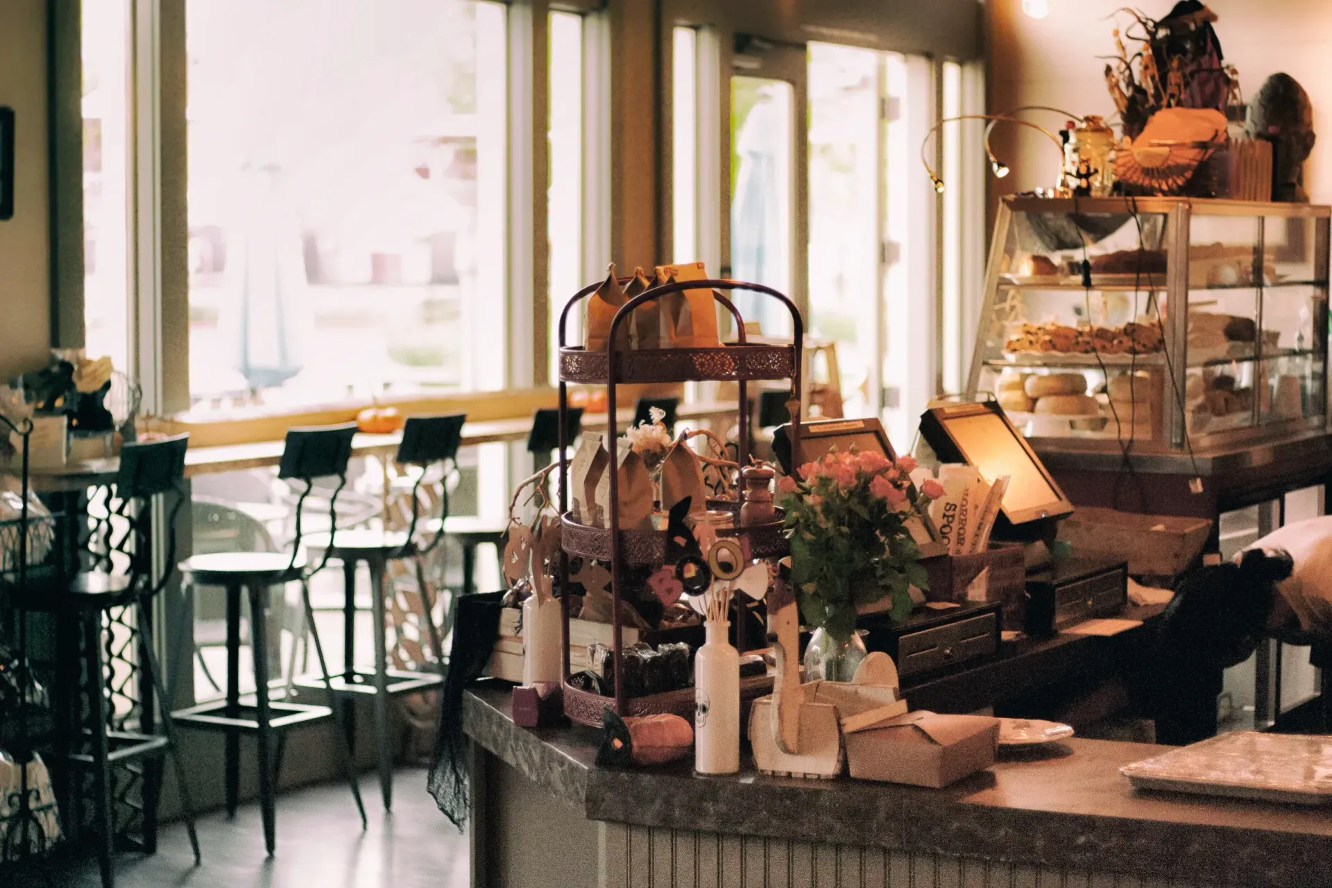 Cafe interior with countertop display of pastries and floral arrangements by a window.