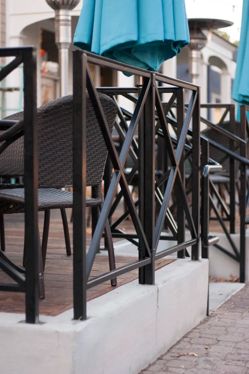 Black metal fence with crisscross design, enclosing a patio with blue umbrellas and seating.