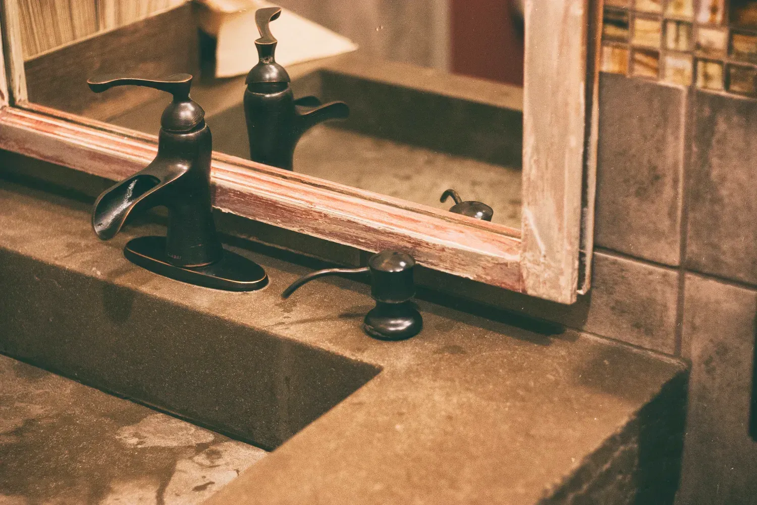 Dark faucet and soap dispenser on a concrete sink, reflected in a mirror.