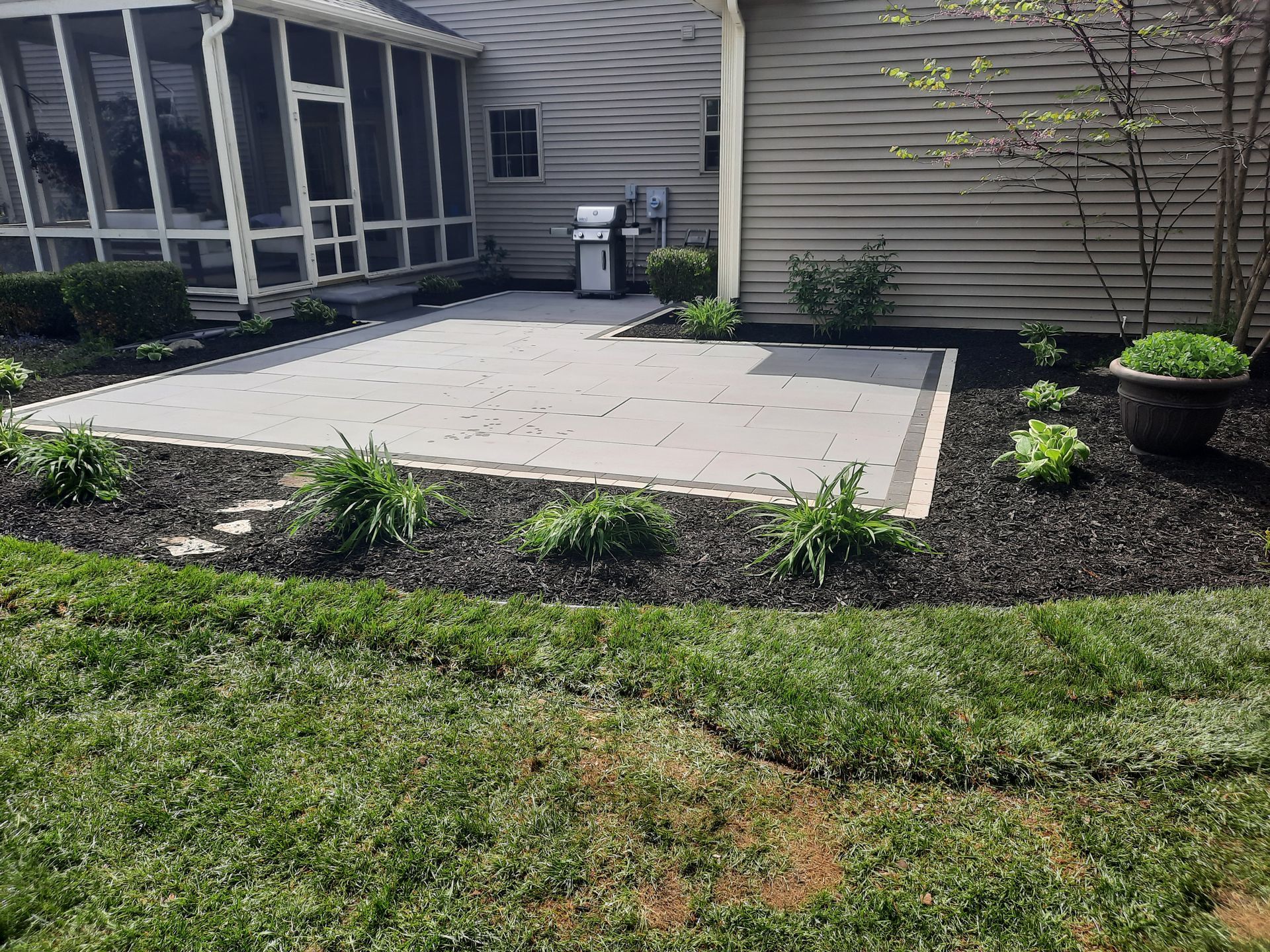 A patio with a grill and a screened in porch in the backyard of a house.