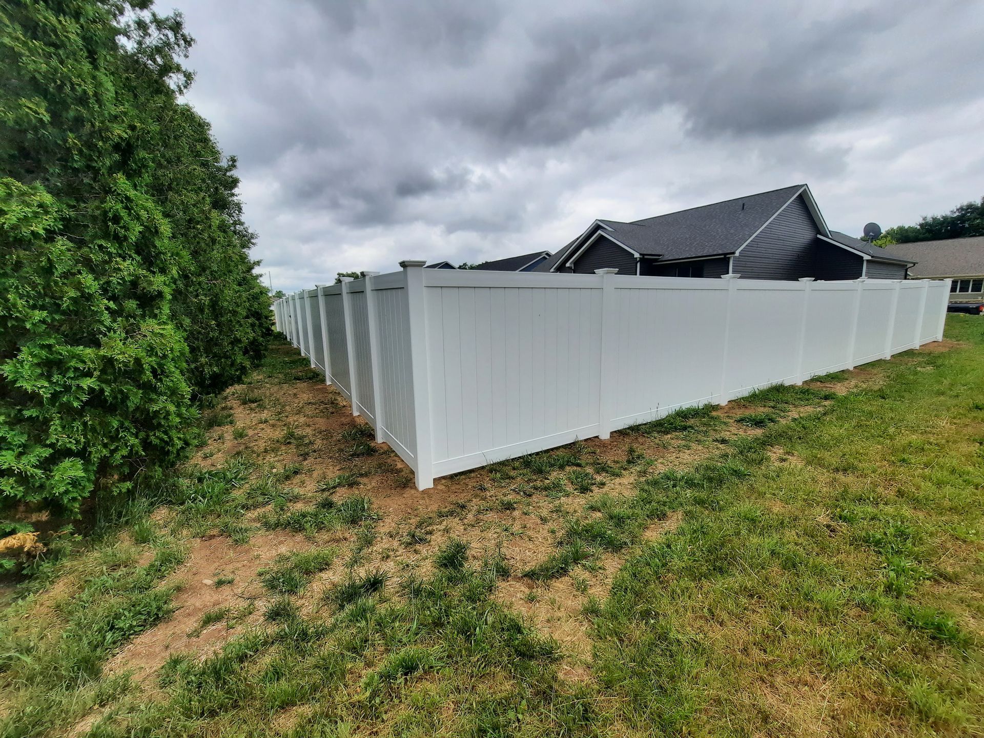 A white fence surrounds a grassy field in front of a house.