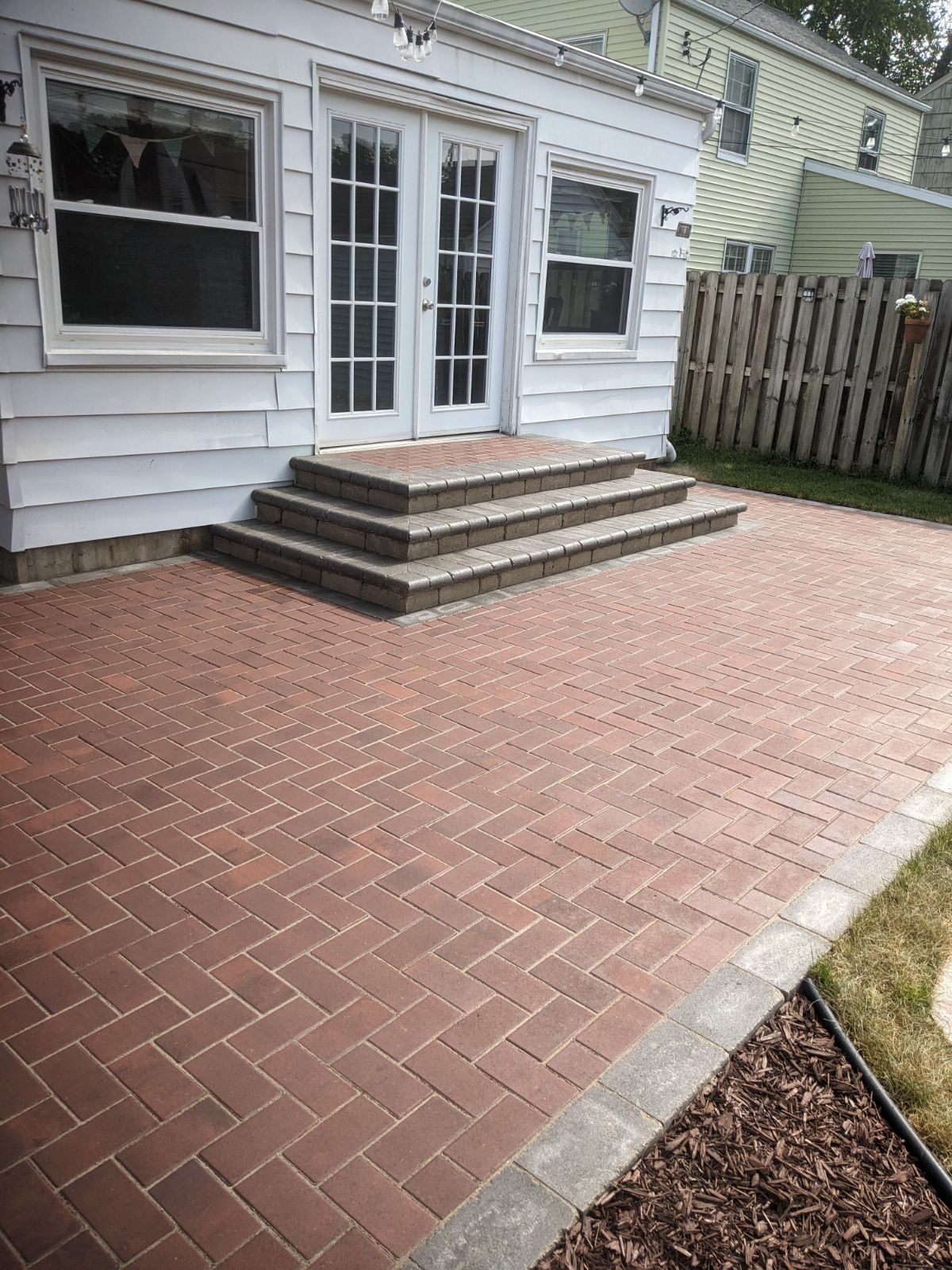 There is a brick patio in front of a house with stairs leading up to it.