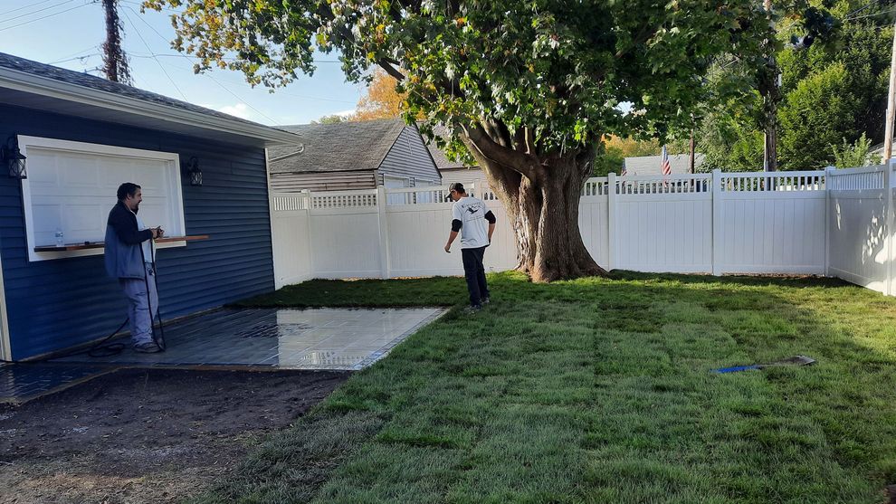 Two men are standing in a backyard with a white fence.