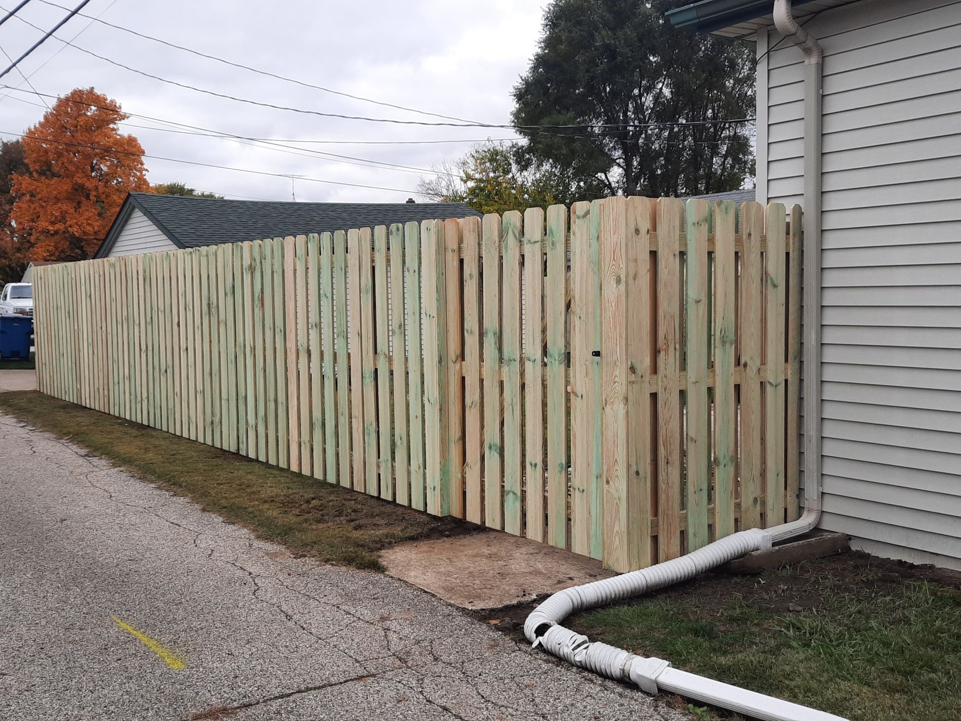 A wooden fence is sitting next to a house on the side of the road.