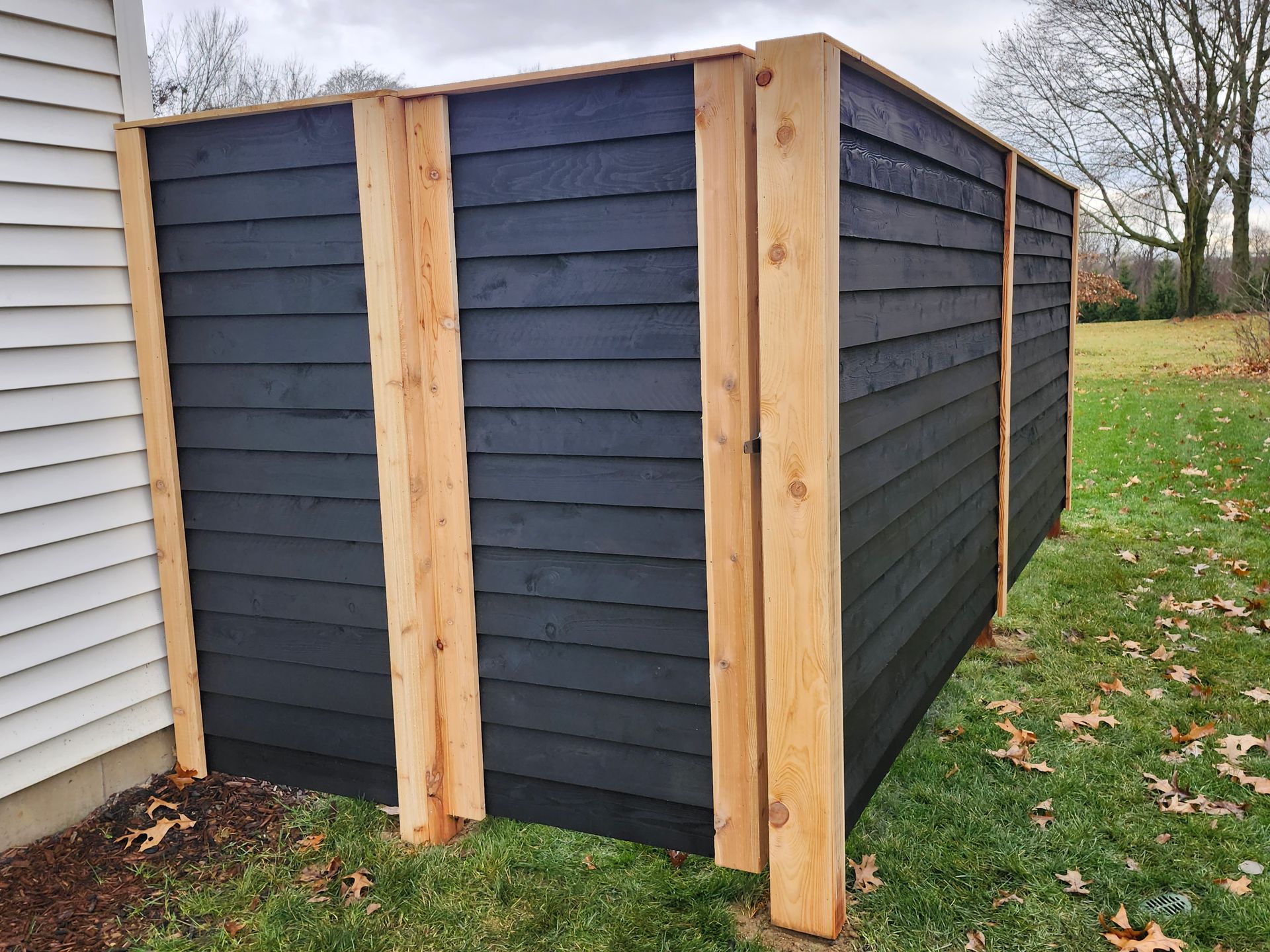 A black wooden fence is sitting in the grass next to a white house.