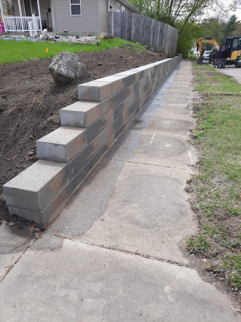 A concrete wall is being built next to a sidewalk next to a house.