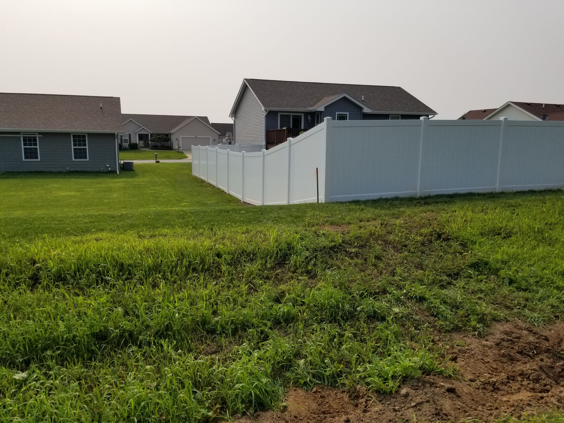 A white fence surrounds a lush green field with houses in the background.
