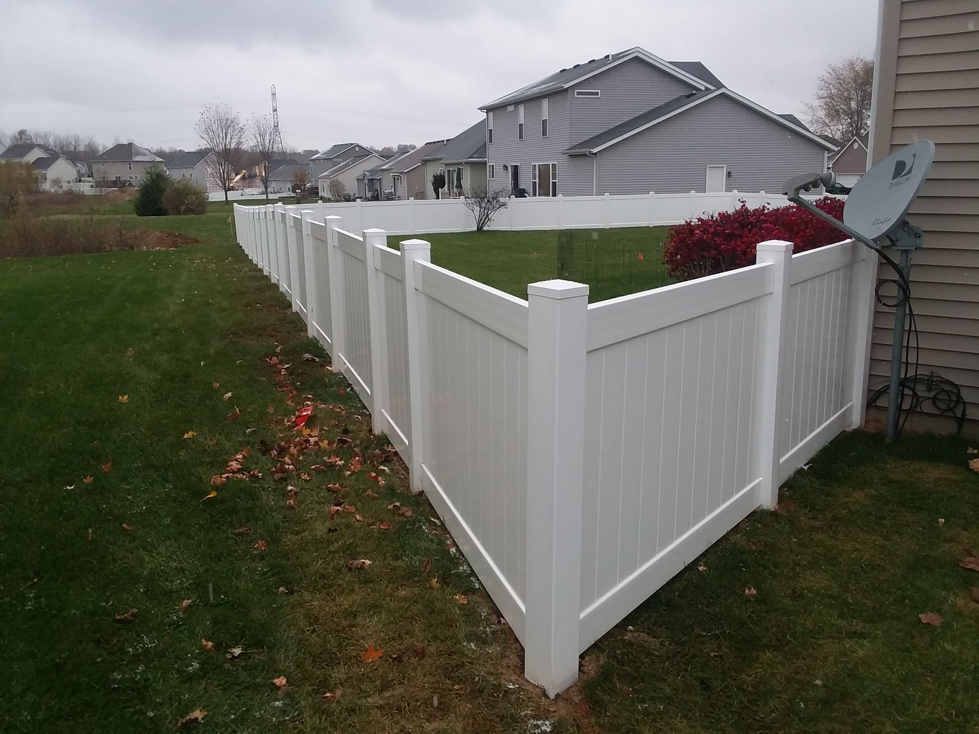 A white fence surrounds a lush green yard in front of a house