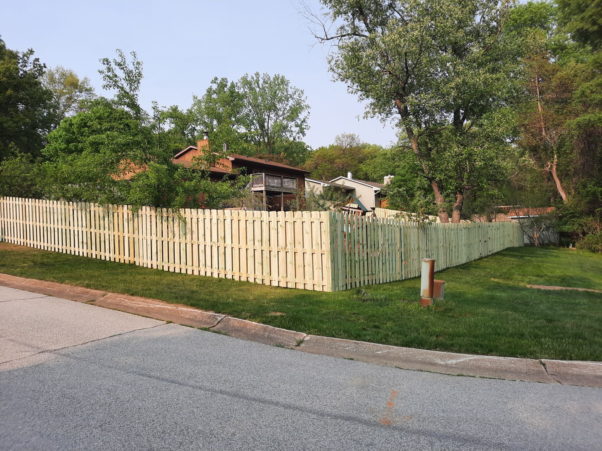 A wooden fence surrounds a lush green yard in front of a house.