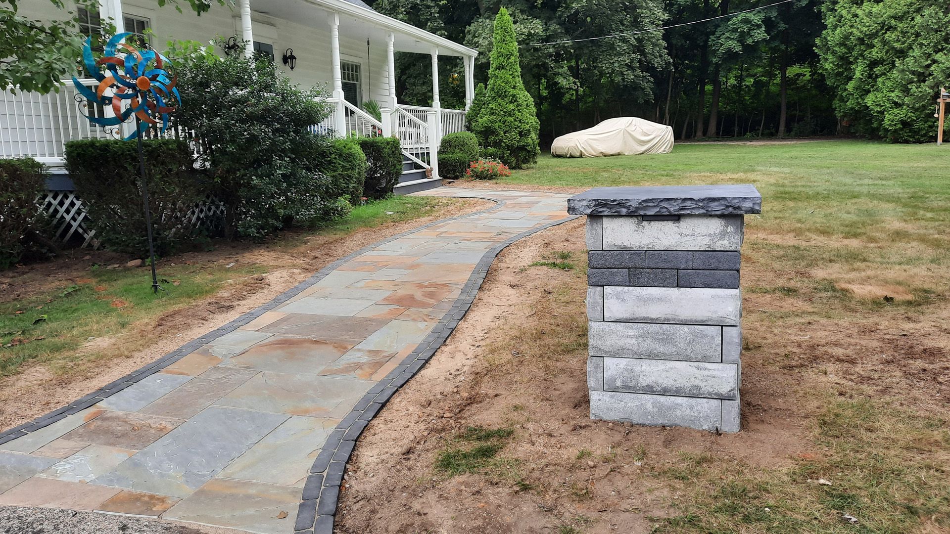 A stone walkway leading to a house with a brick pillar in front of it.