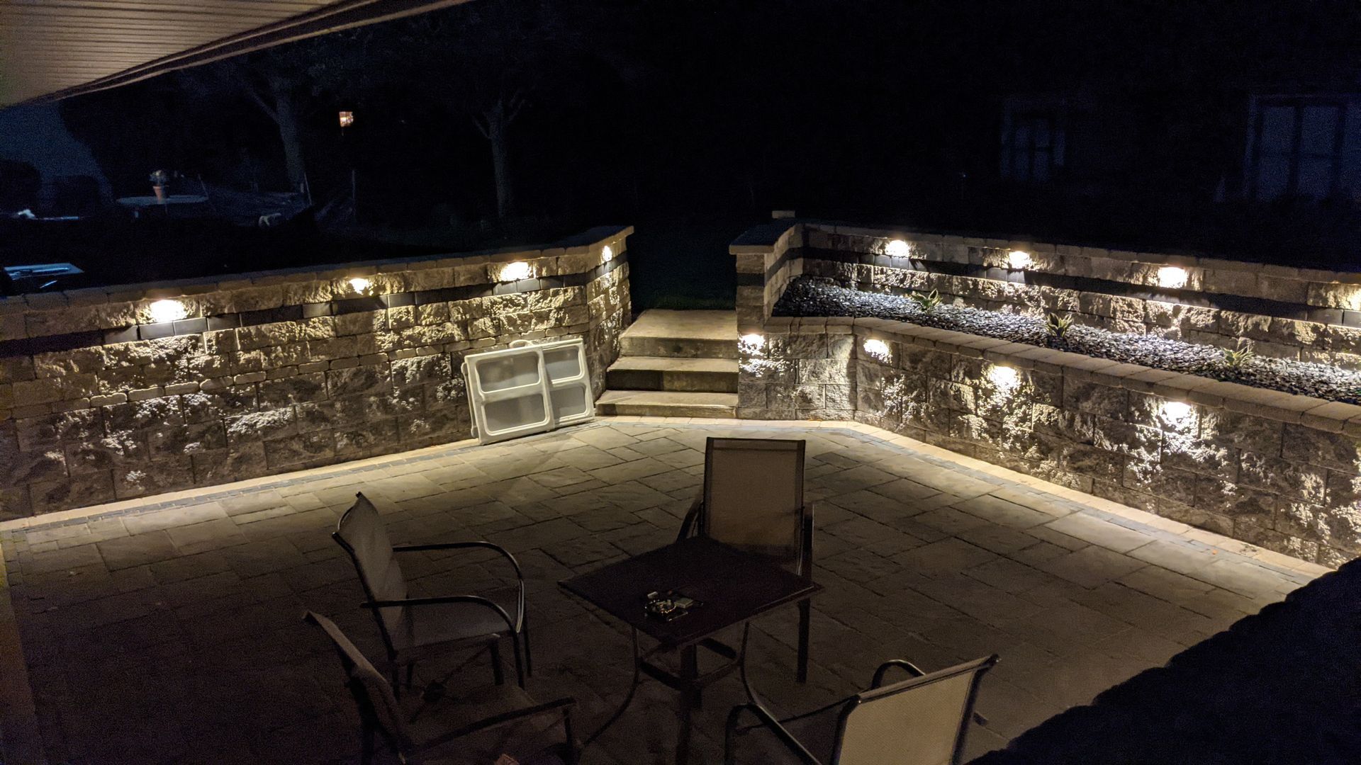 A patio with a table and chairs is lit up at night.