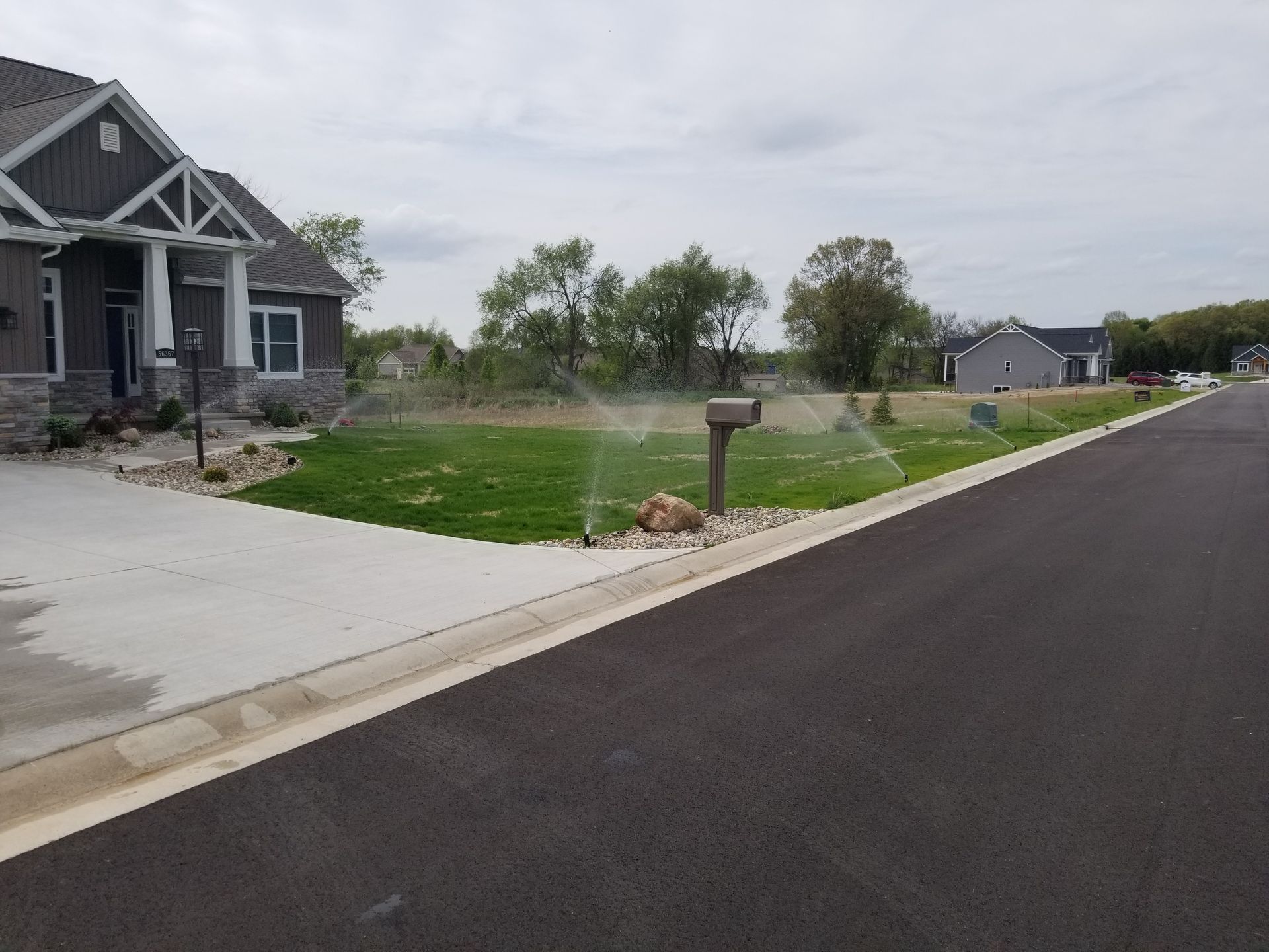 A sprinkler is spraying water on a lush green lawn in front of a house.