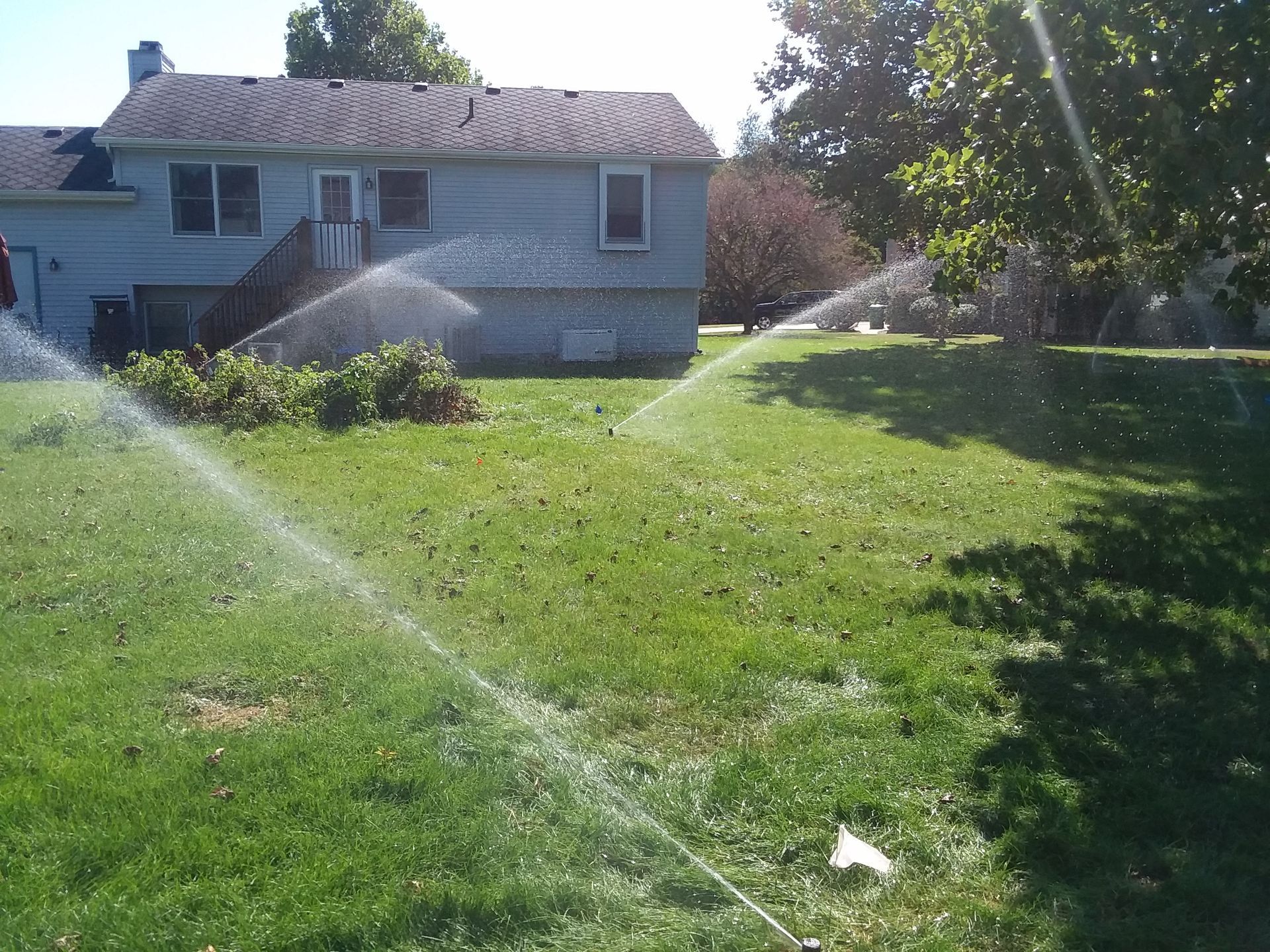 A sprinkler is spraying water on a lush green lawn in front of a house