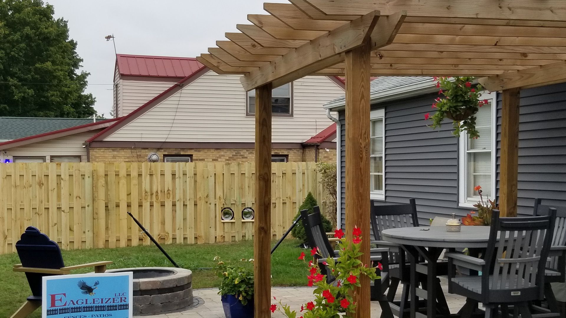 A wooden pergola over a patio with a fire pit and a table and chairs.