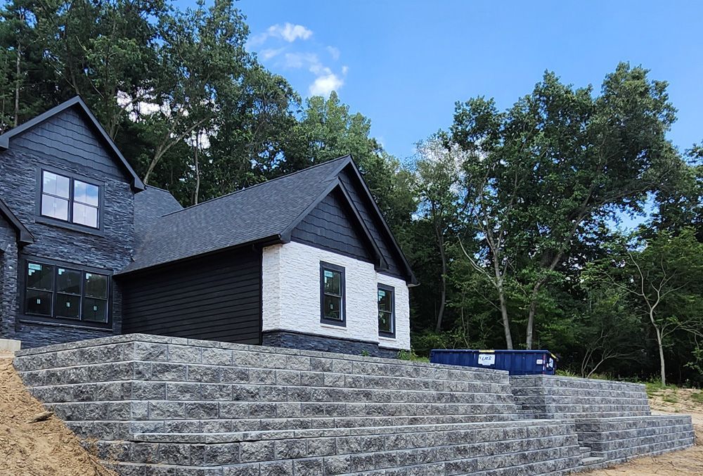 A black and white house is sitting on top of a hill surrounded by trees.