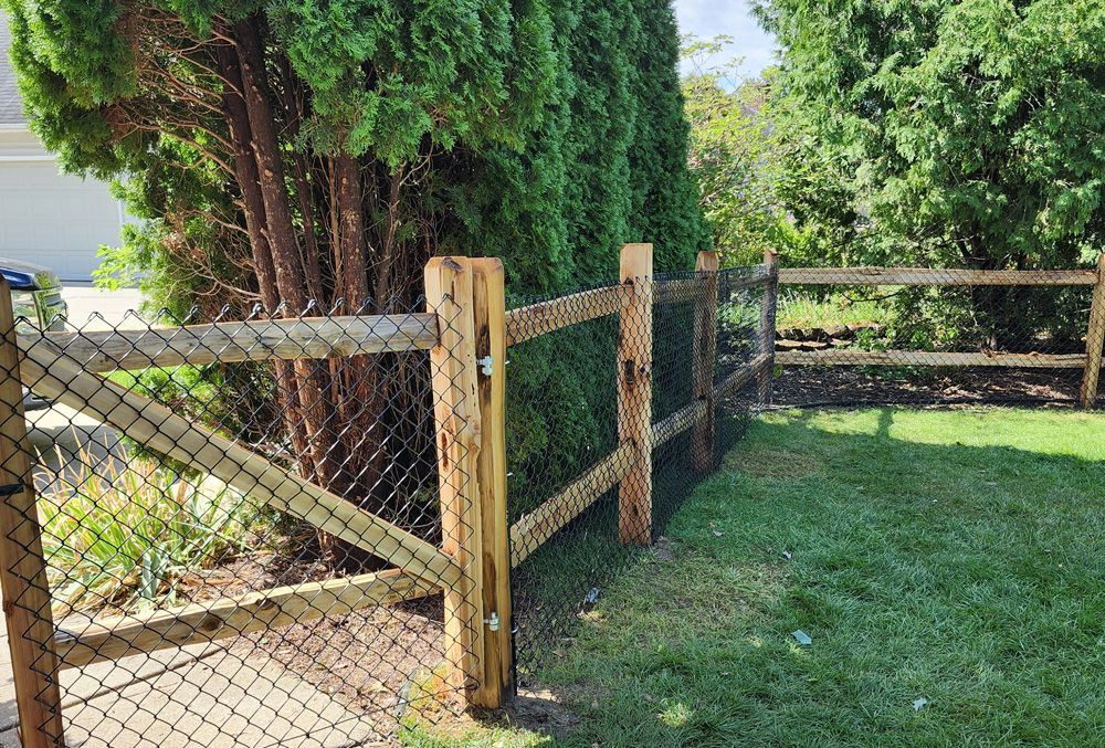 A wooden fence with a chain link fence surrounding a lush green yard.