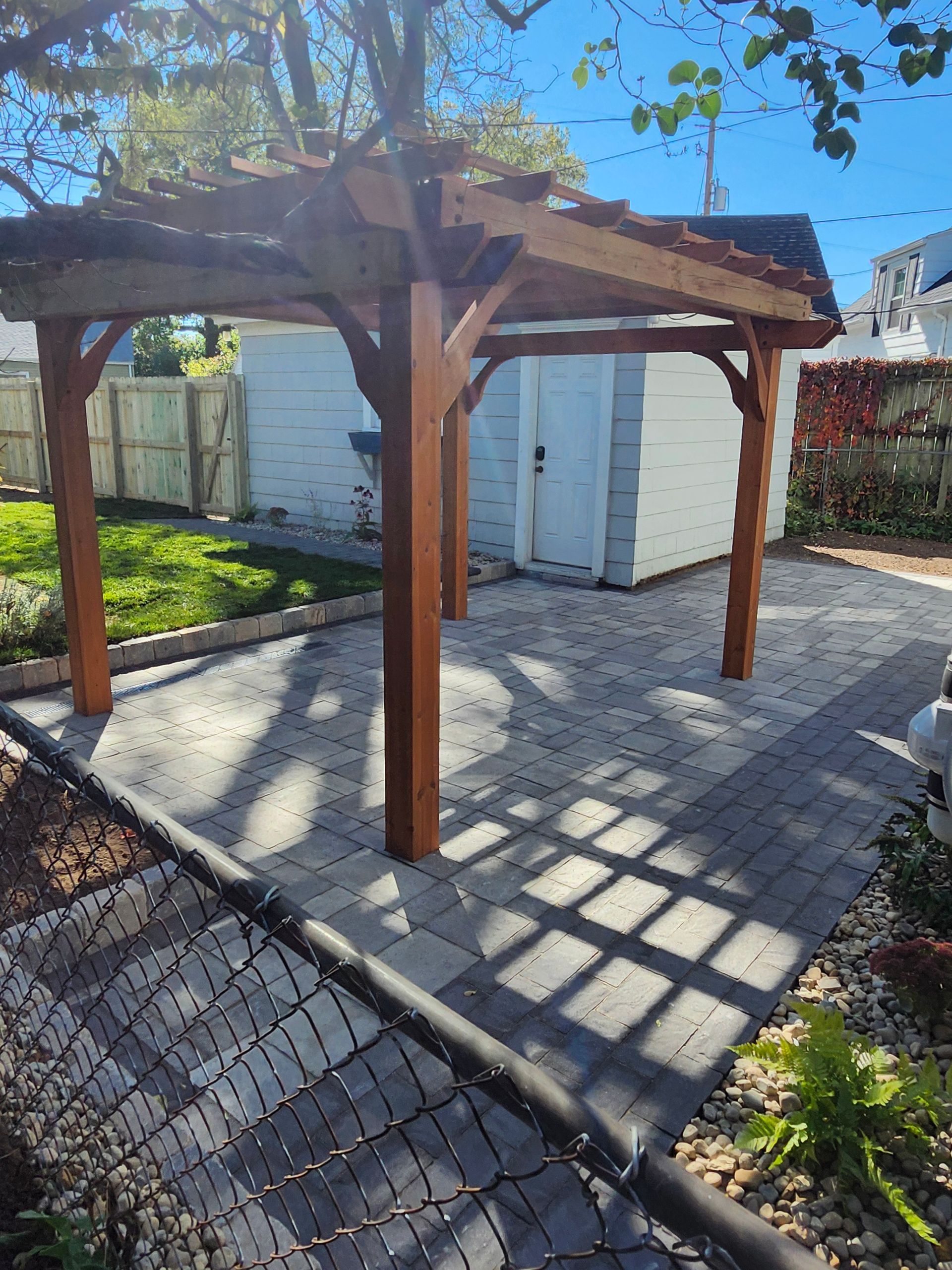 A wooden pergola is sitting on top of a brick patio in a backyard.