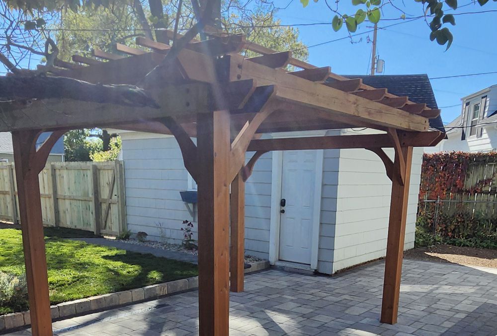 A wooden pergola is sitting in front of a white garage.