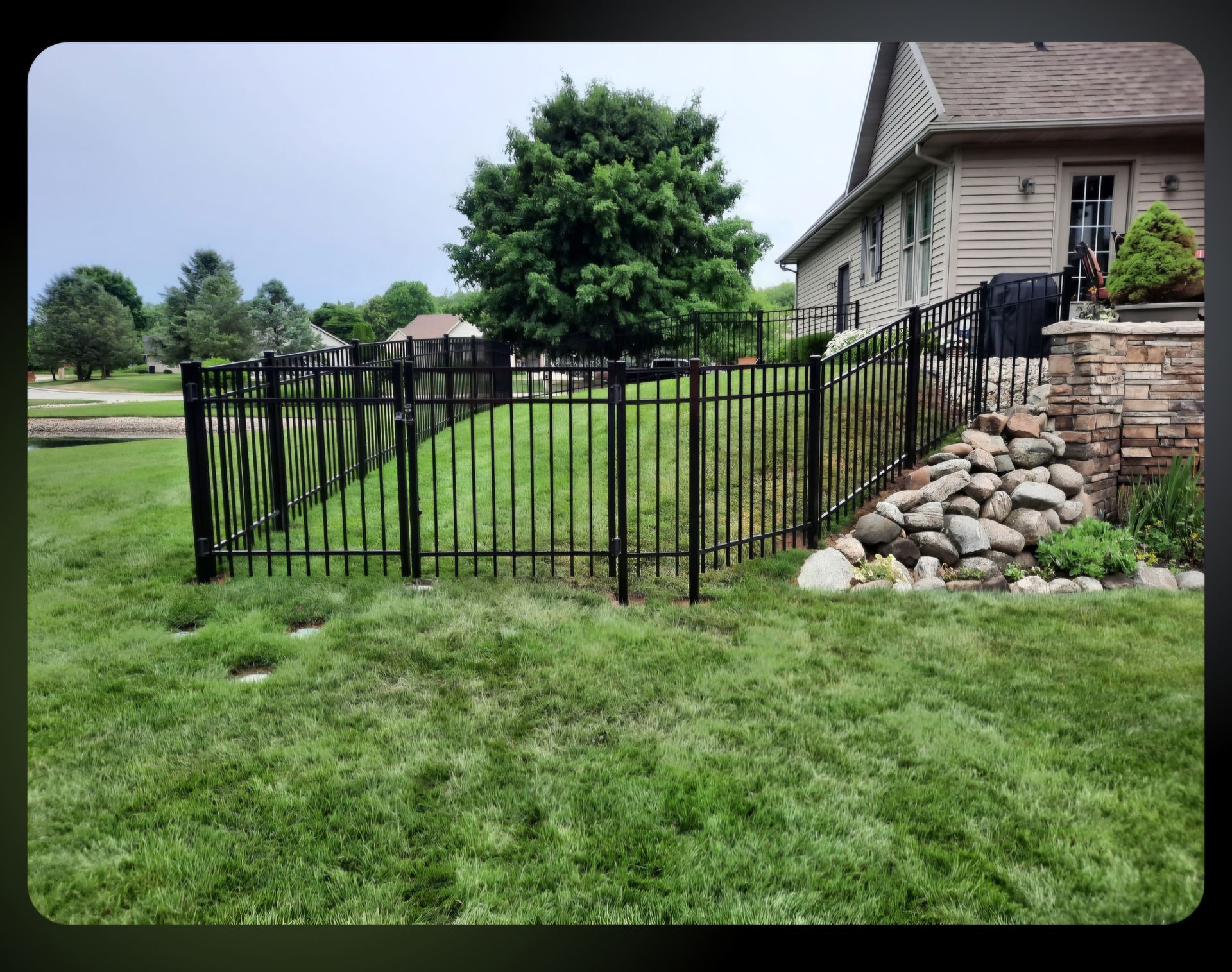 A black fence surrounds a lush green yard in front of a house
